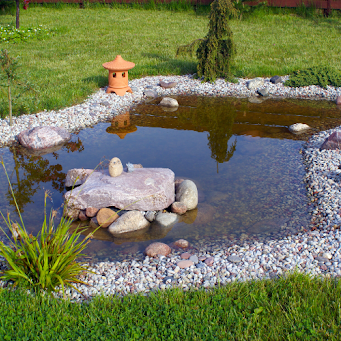 A small garden pond surrounded by gravel, rocks, and grass.