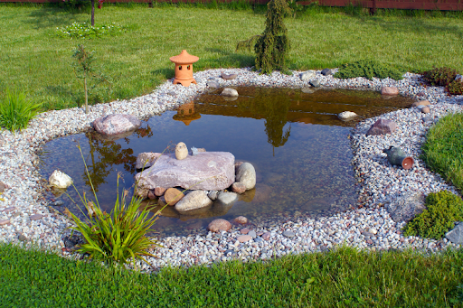 A small garden pond surrounded by gravel, rocks, and grass.