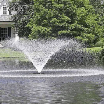 A pond fountain spraying water in front of a house and trees.