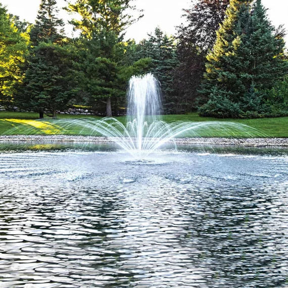 Airmax EcoSeries 1/2 HP pond fountain with crown and trumpet spray pattern in a pond with pine trees in the background