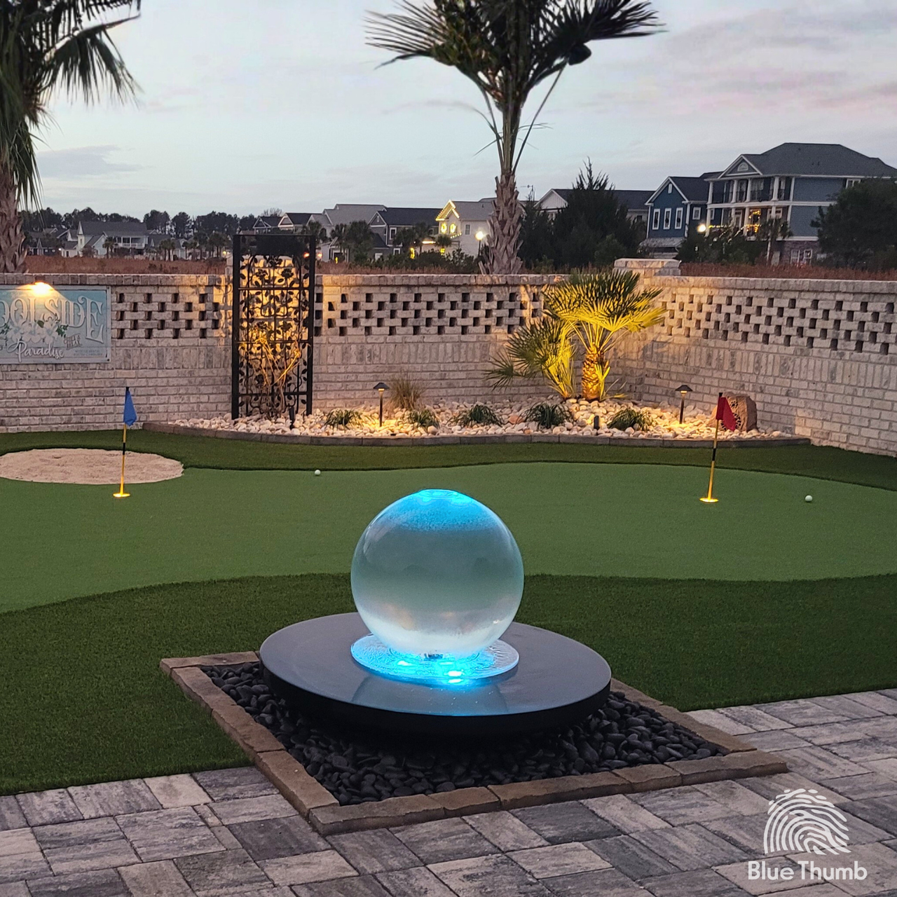 Crystal sphere fountain glowing blue with color-changing LED lights at dusk