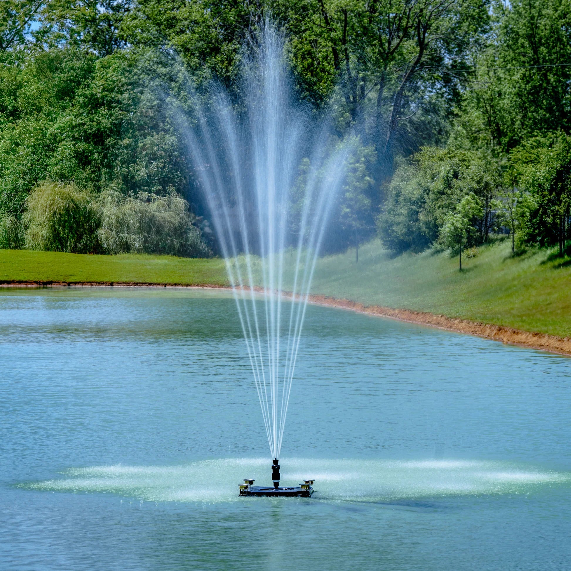 Outdoor Water Solutions Classic Fountain in a lake with trees and grass in the background