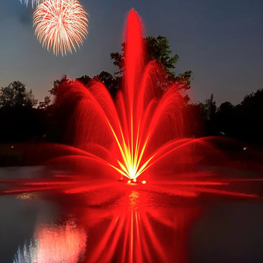 Outdoor Water Solutions Classic Fountain with Red LED lights show with fireworks in the sky over a lake