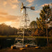 Outdoor Water Solutions four legged metal aerating windmill  against a sunset sky with trees in the background