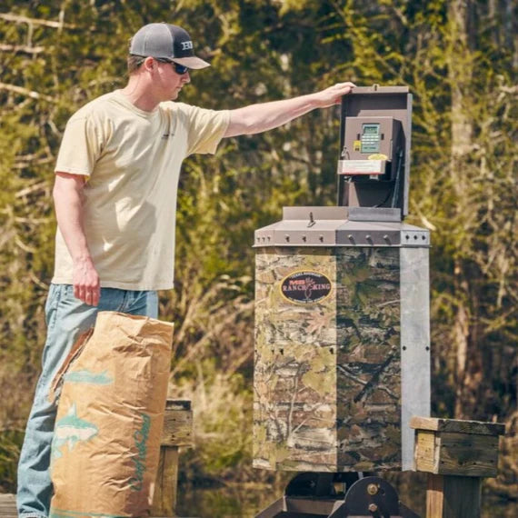 Man interacting with a Texas Avenger Fish Feeder in a forest setting