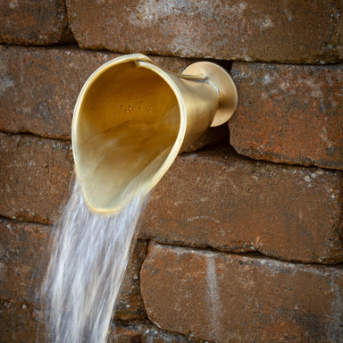 Brass Calla Lily flower spout flowing from a garden wall